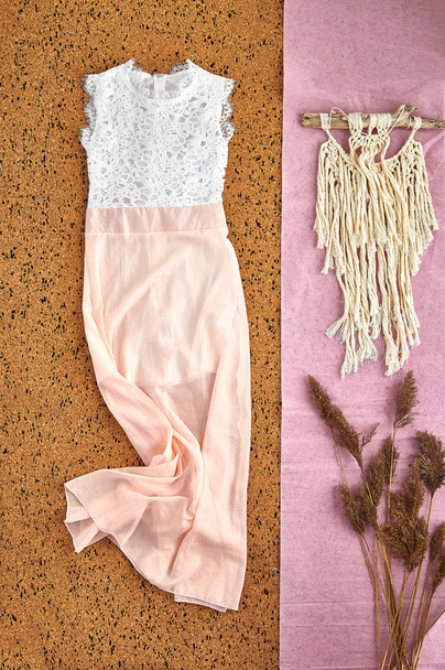 Hermosa presentación de ropa inusual para el blog de moda, publicidad, catálogo de ropa. Delicado vestido rosa hecho de tela transparente con un corpiño de encaje blanco. Atrapasueños y espiguillas secas
. - Foto, Imagen