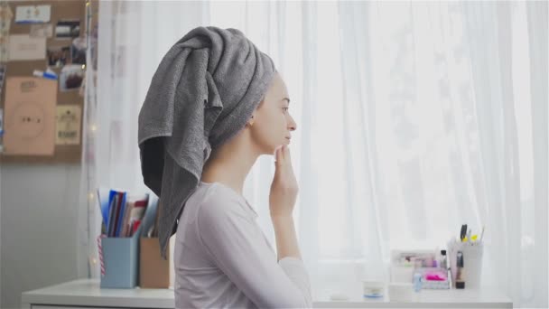 Una joven limpia la piel de la cara con una almohadilla de algodón en la habitación
 - Metraje, vídeo