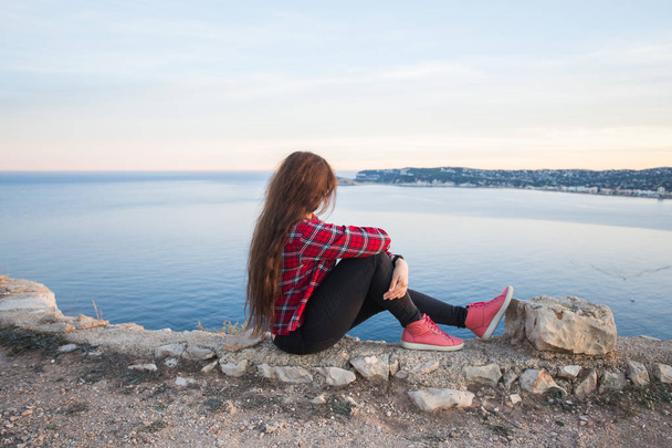 Путешествия, приключения и одиночество концепции - девушка сидит на краю скалы и смотрит на море
 - Фото, изображение