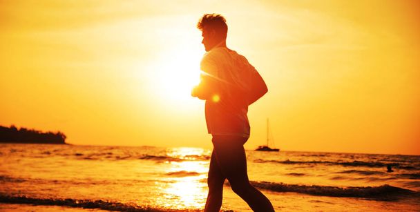 Muskularny mężczyzna jogging na tropikalnej plaży - wieczorne ćwiczenia - Zdjęcie, obraz
