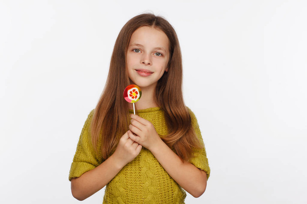 Emotional portrait of an eight-year girl in a yellow-green sweater and with a lollipop in her hands - Foto, imagen