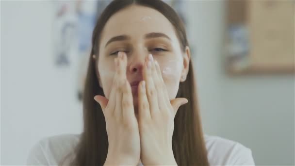 Woman applying mask moisturizing skin cream on face and look at the camera - Felvétel, videó