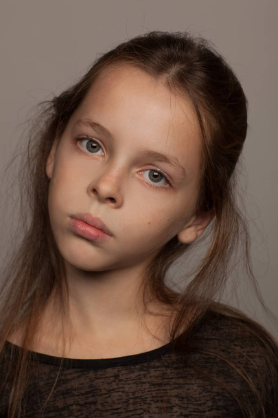 Portrait of an eight-year-old girl with a calm mood, in a black blouse and with picked up hair. Studio photo session. Gray background - Zdjęcie, obraz