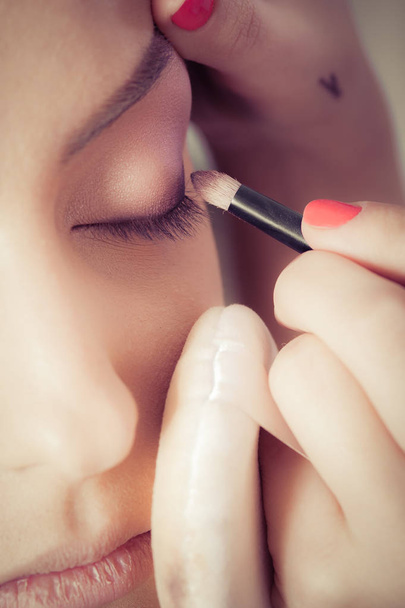 Closeup of hands applying eyeshadow powder on female facial skin - Фото, изображение