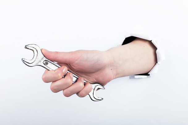 Female hand out of a hole in paper, holds a wrench. Isolate on white background to labor day. - Photo, image