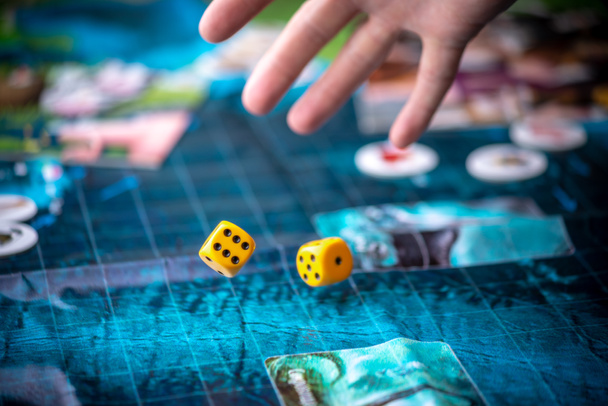 Hand throws two yellow dice on the blue field of the fantasy game. Gaming moments in dynamics. Board games strategy - Photo, Image