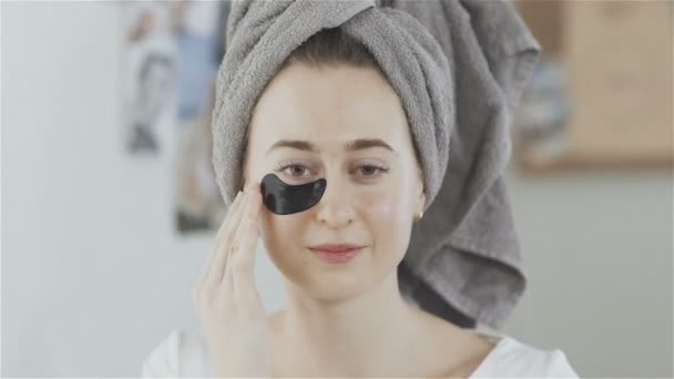 Woman with towel on head imposes under eyes patches of a refreshing Collagen hydrating mask. - Filmmaterial, Video