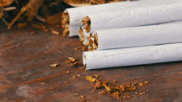 Domácí cigarety nebo roll-up s tabákem jsou na stole vedle suchých tabákových listů - Záběry, video