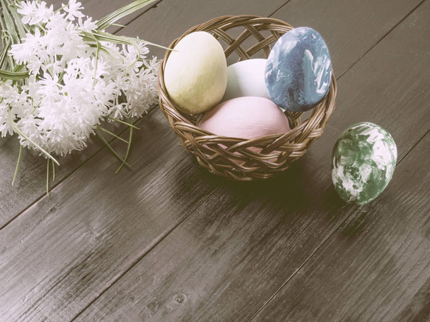 Basket with colorful easter eggs and flower on wooden table - Foto, immagini