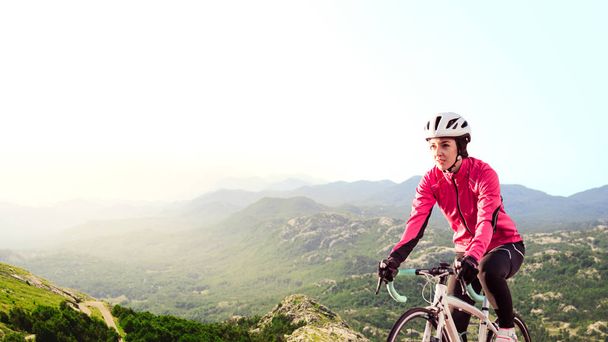 Jonge vrouw in helder roze jas rijden weg fiets op Alpine bergweg. Gezonde levensstijl en avontuur Concept. - Foto, afbeelding