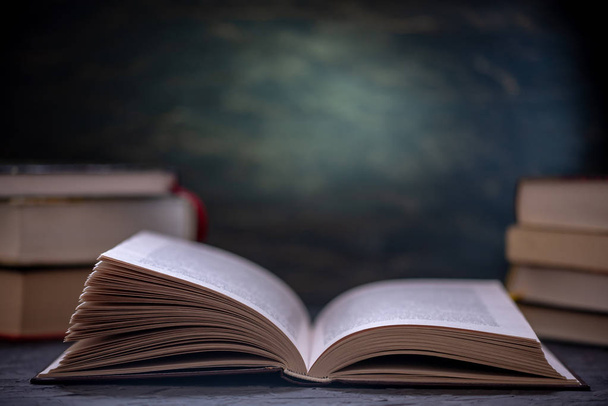 Libro aperto su una pila di libri su un tavolo su uno sfondo scuro. Istruzione e lettura di libri cartacei
 - Foto, immagini