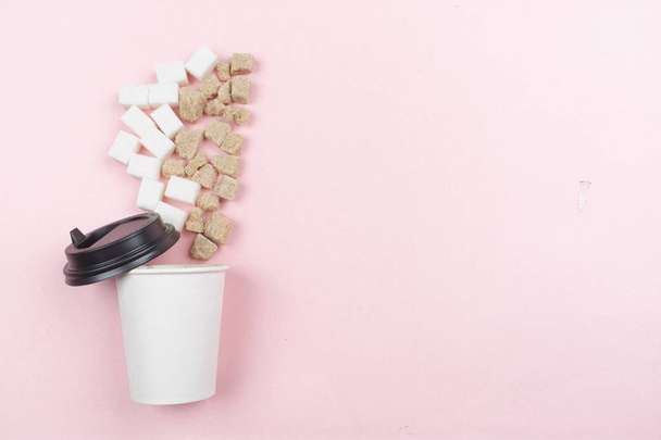 Suikerklontjes in een kopje koffie op een roze achtergrond van papier - Foto, afbeelding