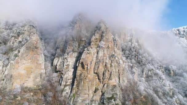 Enorme, oude cliffs op een berghelling vallende struiken en bevroren naaldbomen in grijze wolken tegen blauwe hemel. Schot. Prachtig uitzicht. - Video