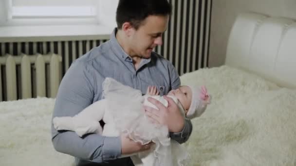 Young dad cradles a little girl on a bed. - Felvétel, videó