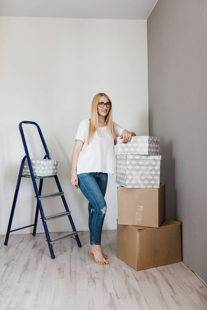 Young woman moving in her new house and doing a home makeover, she is standing near many cardboard boxes around - 写真・画像