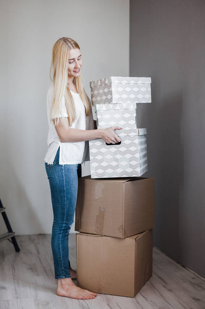 Young woman moving into new apartment holding cardboard boxes with belongings.Photo of young blonde with cardboard box. - Fotografie, Obrázek