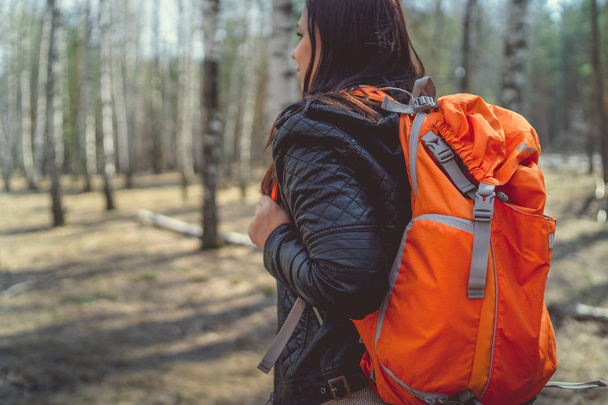 Traveling woman with backpack in woodsSide view of brunette standing with bright orange backpack in tranquil sunny forest looking away - Photo, Image