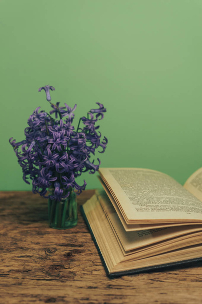 Açık bir kitap ve bir eski meşe ahşap masa mor çiçek. Yeşil duvar arka plan. - Fotoğraf, Görsel