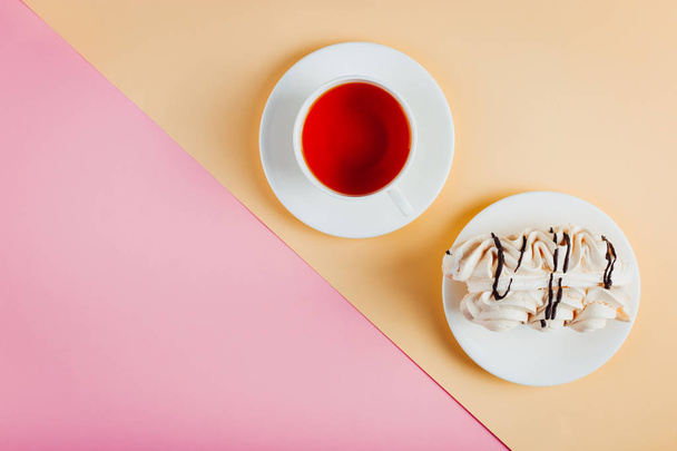 Meringue cake on a saucer and a cup of tea on pastel colored paper background. Copy space. - Valokuva, kuva