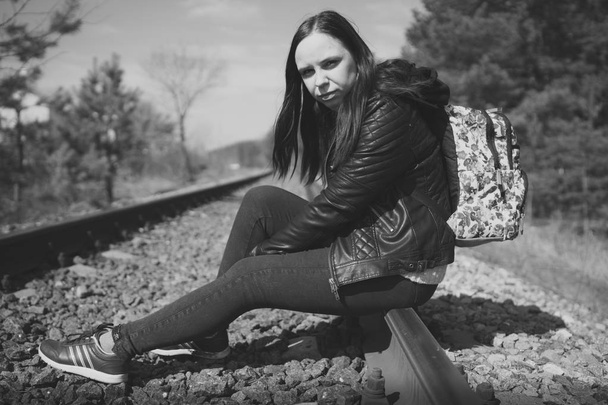 Pensive woman sitting on railway. Side view in black and white of young thoughtful woman sitting on rail and looking away in nature - Photo, image