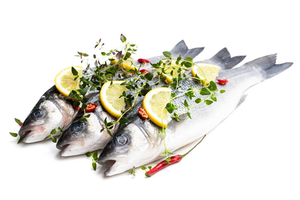 Verse hele zeebaars vissen met citroen en kruiden geïsoleerd op een witte  - Foto, afbeelding