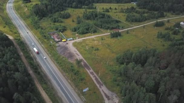 Aerial view on carriageway with moving cars between green dense forest and a small snack bar near the wooden house. Clip. Driving a car - Footage, Video
