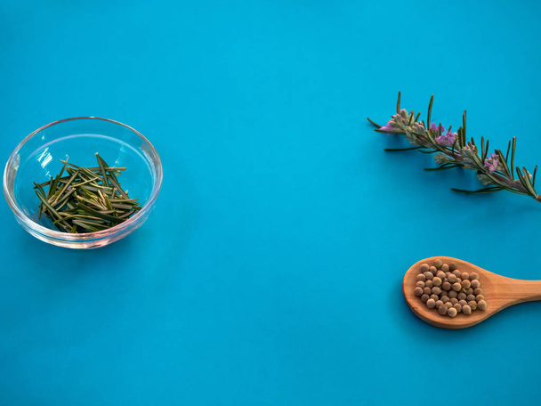 Cuillère en bois avec grains de poivre blanc et romarin sur fond bleu
 - Photo, image