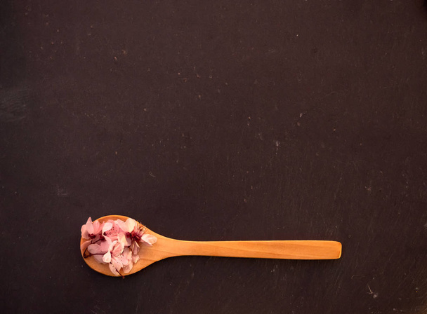 Una cuchara de madera con flores comestibles en un plato de pizarra
 - Foto, Imagen