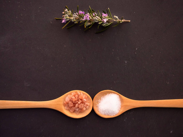 Cucchiai di legno con sale marino comune e sale himalayano rosa e un rametto di rosmarino su un piatto di ardesia
 - Foto, immagini