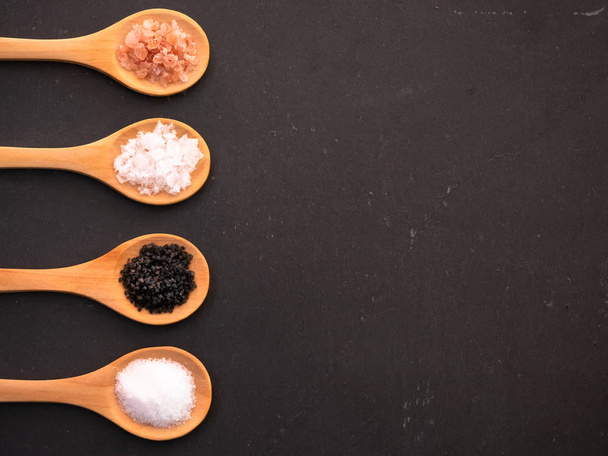 Ξύλινα κουτάλια με αλάτι Ιμαλαΐων, μαύρο αλάτι awaii, κοινό αλάτι και νιφάδες αλατιού σε πλάκα σχιστόλιθου - Φωτογραφία, εικόνα