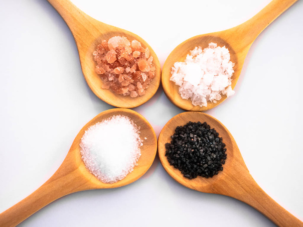 Деревянные ложки с гималайской солью, черная гавайская соль, общие соли и соли хлопья на белом фоне
 - Фото, изображение