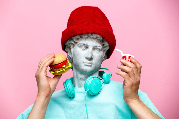 Antieke buste van man in muts met cola drinken en hamburger op roze achtergrond. Klaar voor de zomervakantie - Foto, afbeelding
