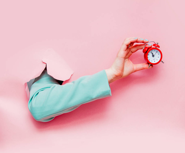 Nainen käsi klassinen sininen takki punainen herätyskello näyttää vaaleanpunainen tausta
 - Valokuva, kuva