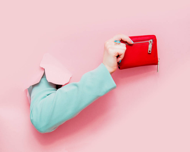 Female hand in classic blue jacket show purse looks out from pink background - Fotó, kép