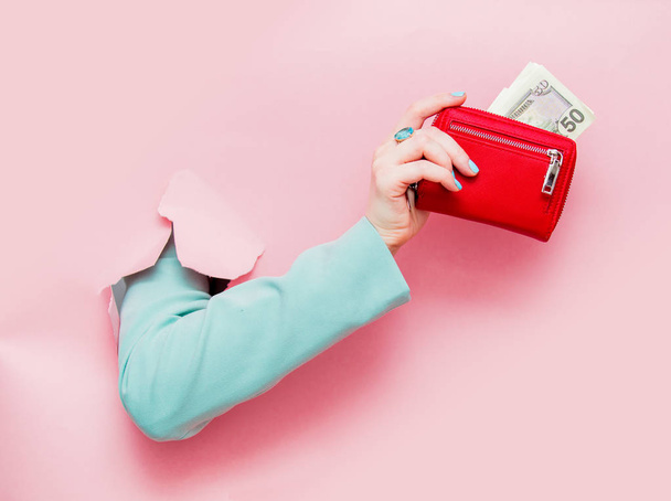 Female hand in classic blue jacket show dollars in purse looks out from pink background - Foto, Imagem