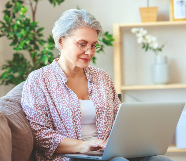 glückliche Seniorin, die zu Hause am Computer-Laptop arbeitet - Foto, Bild
