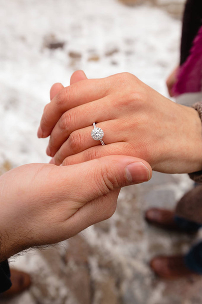 Foto romántica de una linda pareja al aire libre en invierno. Joven que se propone casarse con él con el anillo - Se toman de la mano
 - Foto, Imagen