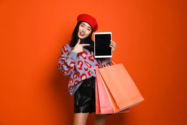 Young asian woman with shopping bags on color background - Foto, afbeelding