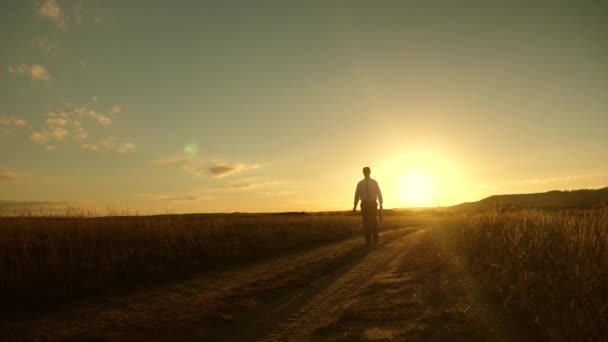 businessman in sunglasses goes down country road with a briefcase in his hand. agricultural business concept. The entrepreneur works in a rural area. farmer inspects the land at sunset. Slow motion. - Footage, Video