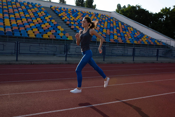 Slender fitness woman running at the stadium at the evening - Fotoğraf, Görsel