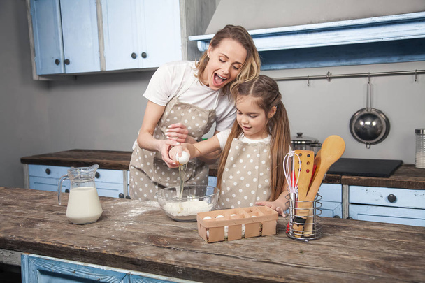 Máma a dcera v kuchyni vařit Mafins. a dcera rozbije vejce nad mouky - Fotografie, Obrázek