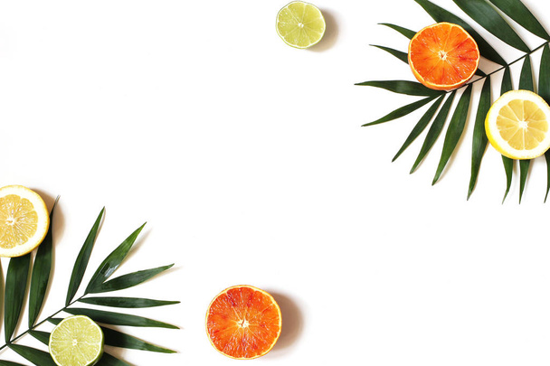 Composición exótica de limones frescos, naranjas rojas, fruta de lima y frondosas hojas de palmeras verdes aisladas sobre fondo de mesa blanco. Concepto de vacaciones tropicales de verano. Asiento plano, vista superior. Marco decorativo
. - Foto, imagen