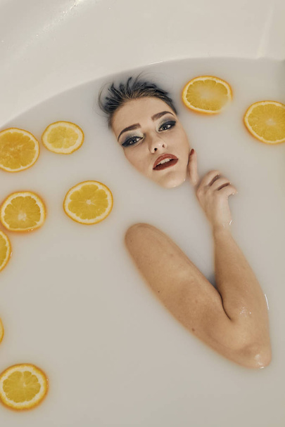 Mujer joven en el baño de leche y con rodajas de naranjas
. - Foto, imagen