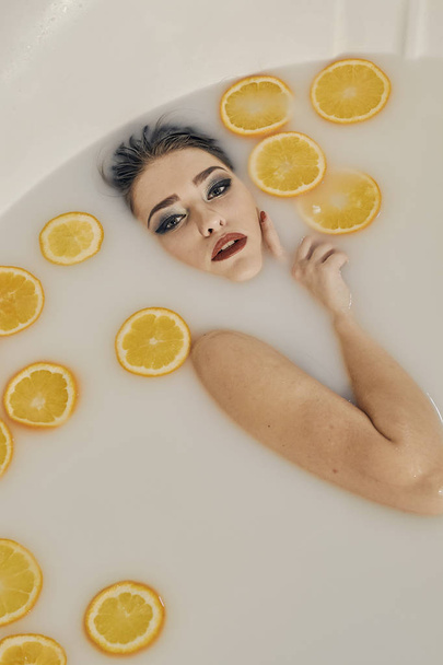 Mujer joven en el baño de leche y con rodajas de naranjas
. - Foto, imagen