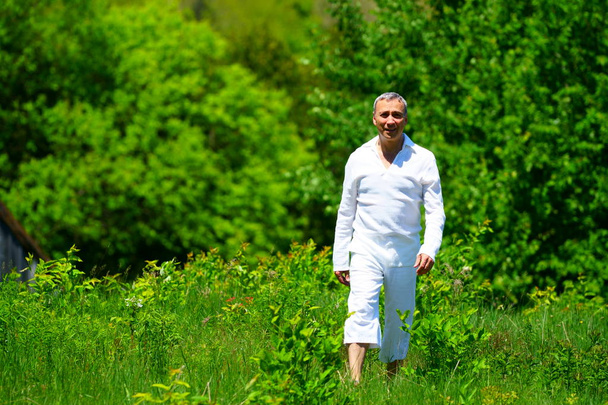 緑に囲まれた野原を歩き、花に触れる白い服を着た男. - 写真・画像