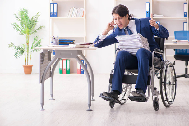 Молодой работник в инвалидной коляске работает в офисе
  - Фото, изображение