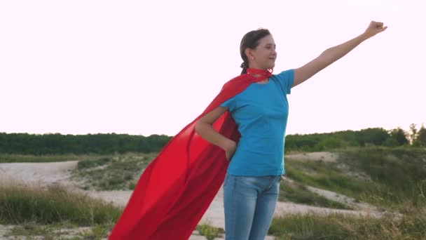 menina sonha em se tornar um super-herói. bela menina super-herói em pé no campo em um manto vermelho, vacilante manto no vento. Movimento lento. menina caminha em um manto vermelho expressão de sonhos
 - Filmagem, Vídeo