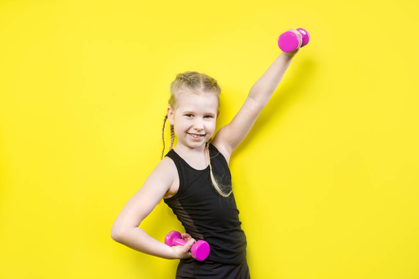 Theme sport and health. Beautiful caucasian child girl with pigtails posing on yellow background with smile. little athlete holding pink dumbbells. Banner for advertising, space for text copy space - Photo, Image
