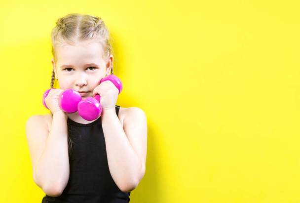 Theme sport and health. Beautiful caucasian child girl with pigtails posing on yellow background with smile. little athlete holding pink dumbbells. Banner for advertising, space for text copy space - Foto, immagini