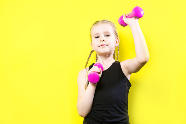 Theme sport and health. Beautiful caucasian child girl with pigtails posing on yellow background with smile. little athlete holding pink dumbbells. Banner for advertising, space for text copy space - Foto, Imagem